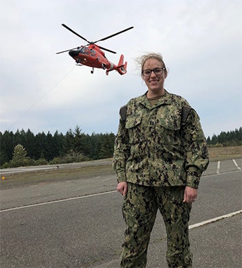 Rebekkah Stoeckler standing on a tarmac in fatigues with a helicopter hovering overhead