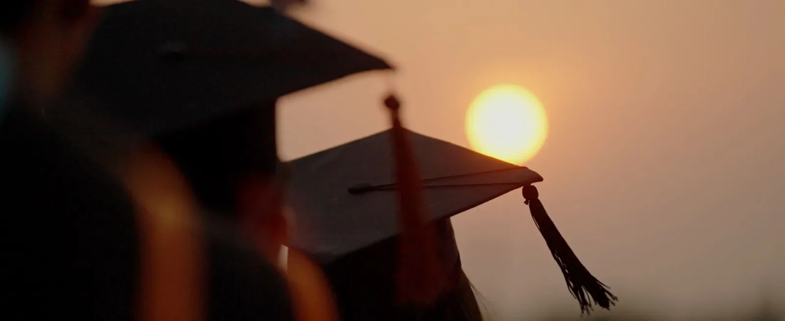 View of graduation caps from behind against sunset